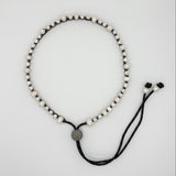 A beaded necklace with small white beads on a black cord, featuring a round gray metal disc at the center and adjustable black cord ends with black beads, shown on a light gray background.