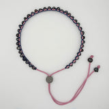 A beaded necklace with dark purple beads and pink macrame cord, featuring a silver-toned round clasp and adjustable sliding cord ends on a white background.