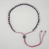 A handmade macrame-style necklace featuring white faux pearls threaded on a navy blue cord, with a pink adjustable cord closure and small pearl beads at the ends.